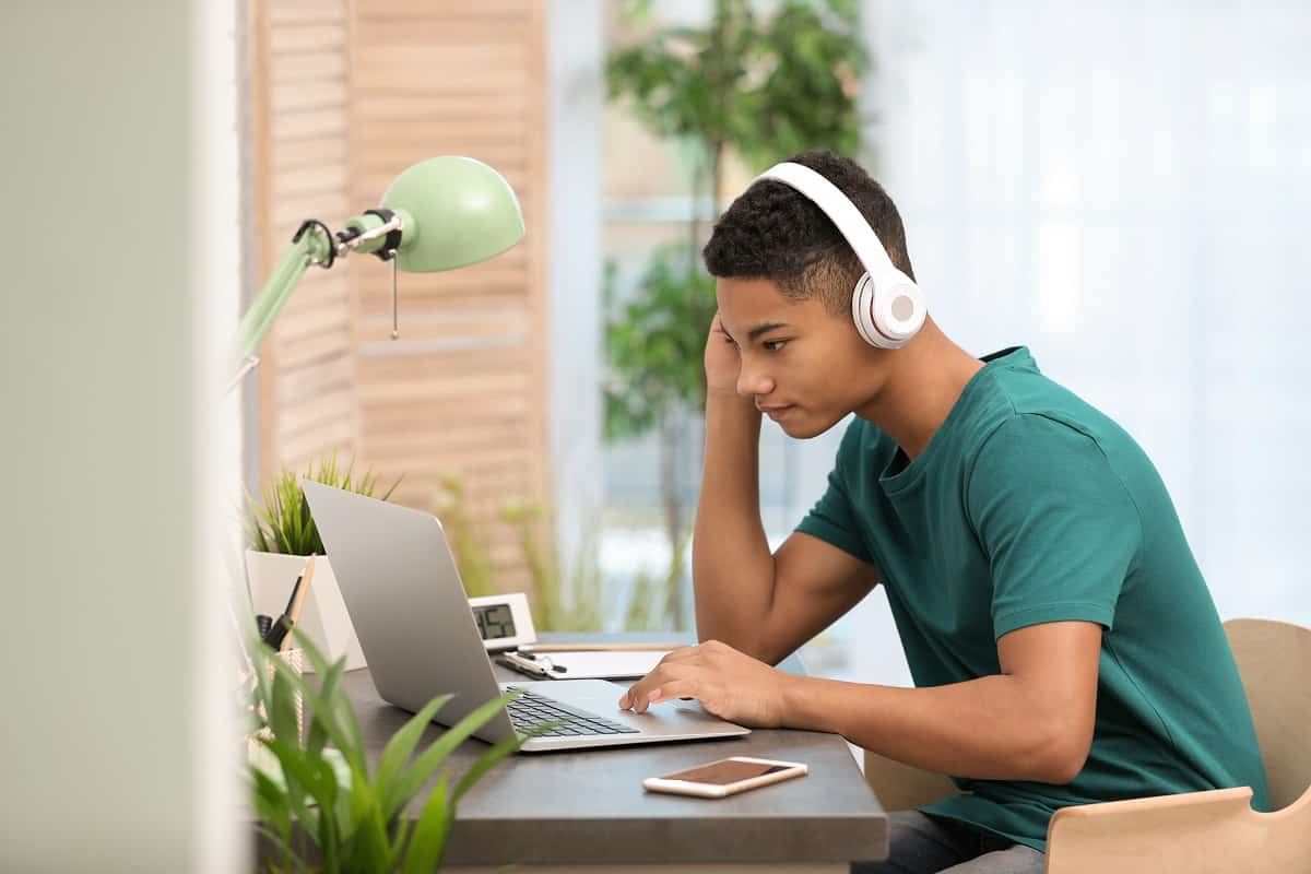 un étudiant avec un casque sur les oreilles et devant un ordinateur portable